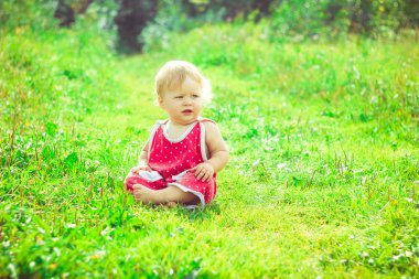 Çocuk çimlerin üzerinde oturuyor.