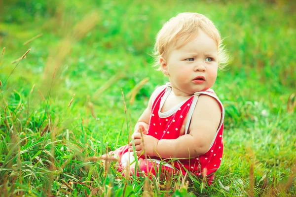 Çocuk çimlerin üzerinde oturuyor.