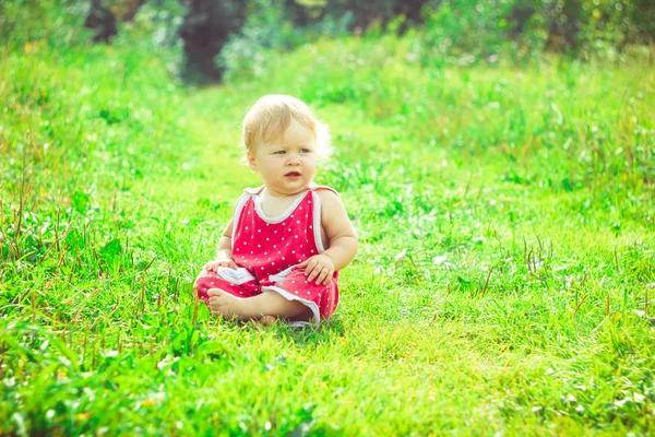 Çocuk çimlerin üzerinde oturuyor.