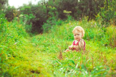 Çocuk çimlerin üzerinde oturuyor.