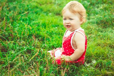 Çocuk çimlerin üzerinde oturuyor.