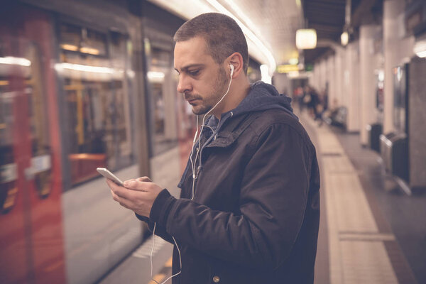 Urban man using smartphone and earphones at the train station 