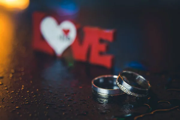 Pair of golden wedding rings and love sign in the background — Stock Photo, Image