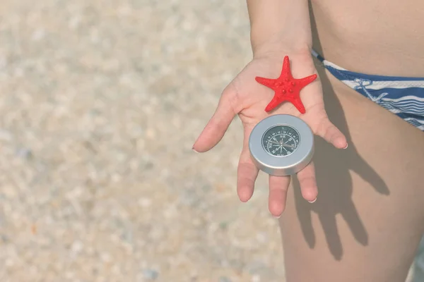 Primo piano della mano femminile che tiene stelle marine e bussola sulla spiaggia. Spazio per la copia . — Foto Stock