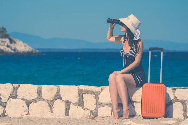 Female tourist with binoculars and luggage at the seaside. Summer vacation and travel concepts. 