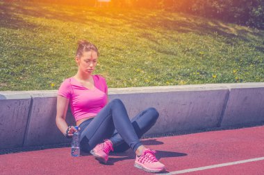 Koşu parkuru üzerinde oturan ve şişe su tutarak koşucu 