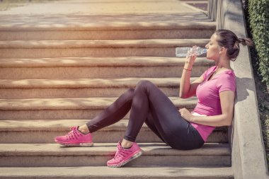 Merdiven ve içme suyu üzerinde egzersiz sonrası oturan koşucu 