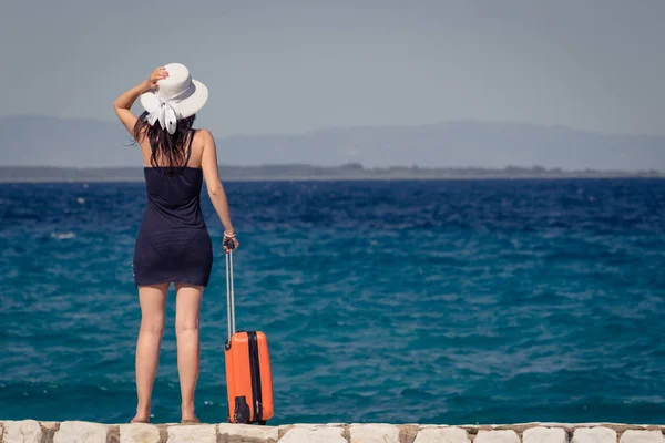 Female tourist with suitcase standing by the sea. Travel and sum