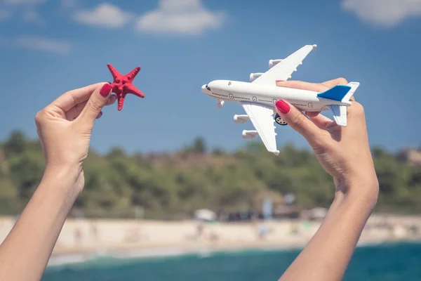 Ženské ruce drží letadlo hračka a sea star proti krásné — Stock fotografie
