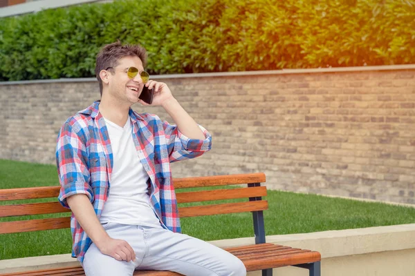 Jonge man zittend op de Bank en het gebruik van smartphone in het park — Stockfoto