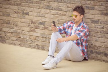 Oturma ve duvara yaslanmış ve smartph kullanarak kentsel adam