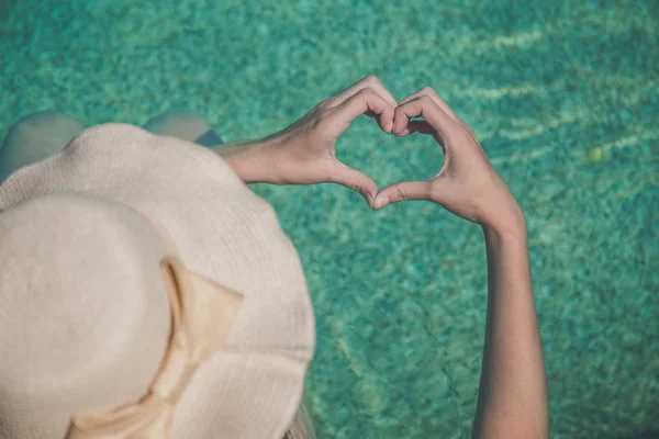 Mujer haciendo forma de corazón con sus manos en la piscina — Foto de Stock
