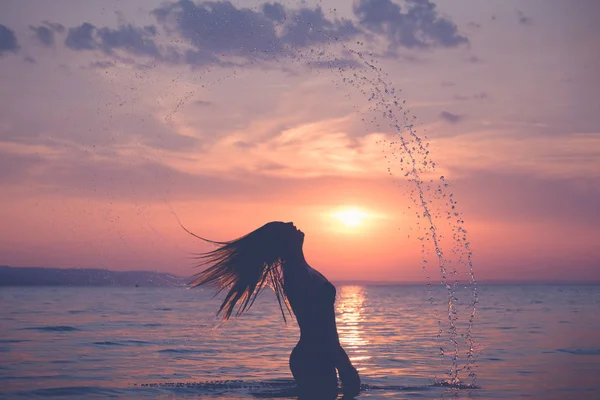 Силуэт женского брызгания водой с волосами на закате — стоковое фото
