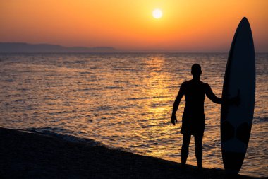 Mutlu sörfçü gün batımında sahilde, sörf tahtaları ile ayakta.