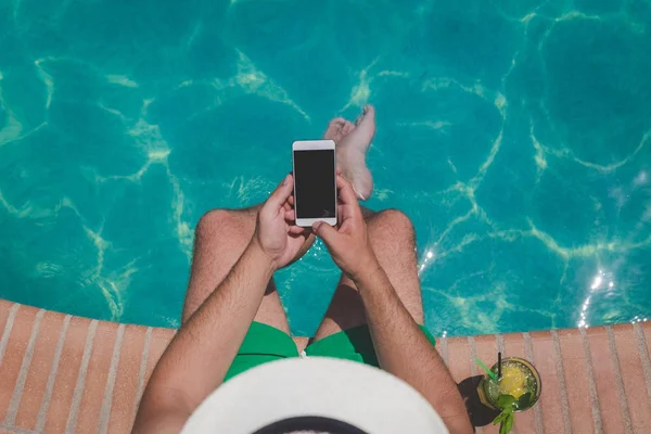 Turista sentado en el borde de la piscina y utilizando la pantalla en blanco — Foto de Stock