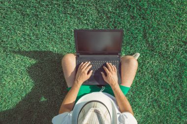 Çimenlerin üzerinde oturan ve boş ekran dizüstü bilgisayar kullanarak bir adam