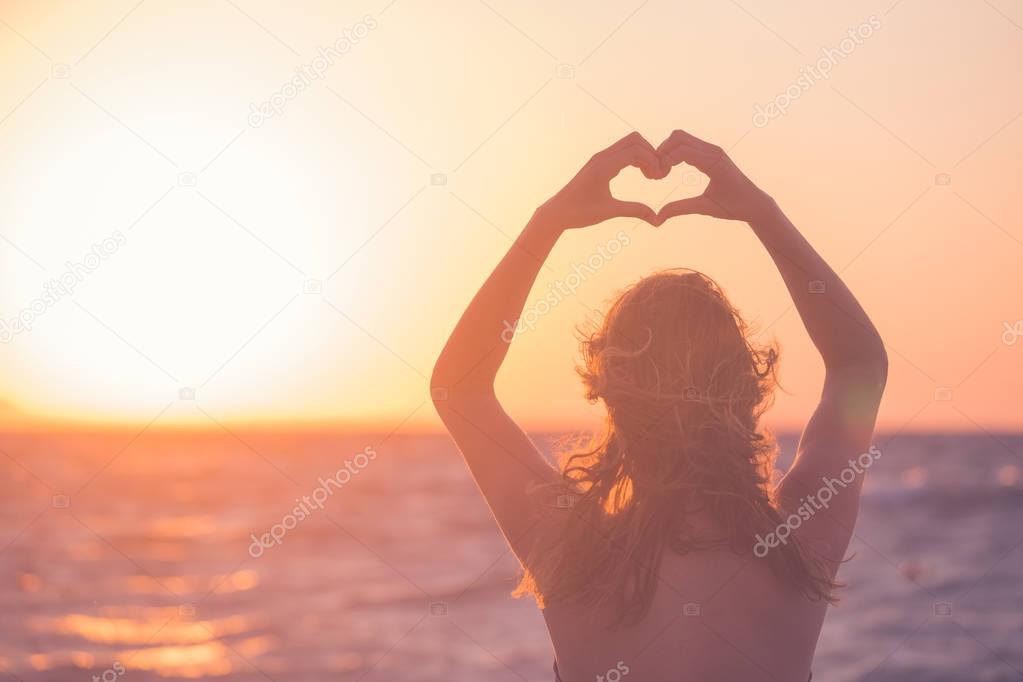Female making heart shape with her hands at sunset over sea