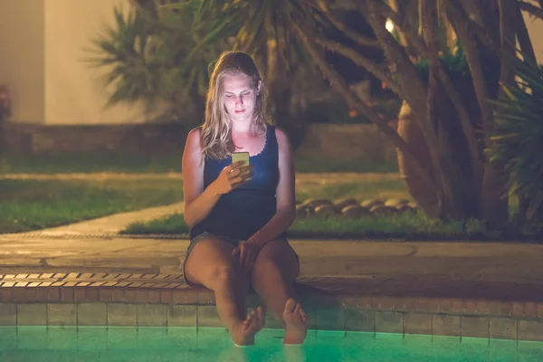 Female using smartphone at the poolside. Night scene.