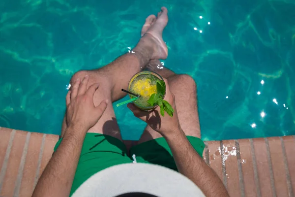 Hombre sentado en el borde de la piscina una celebración mojito cockt — Foto de Stock