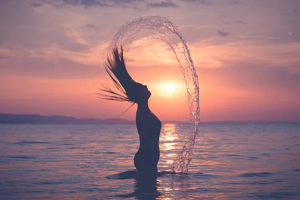Sylwetka kobiece rozpryskiwania wody z jej włosów sunset ove — Zdjęcie stockowe