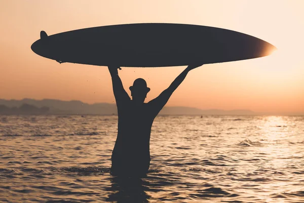 Silhouette dell'uomo che tiene la tavola da surf al tramonto sul mare — Foto Stock