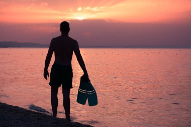 Şnorkel yüzgeçleri kumsalda gün batımında tutan adam