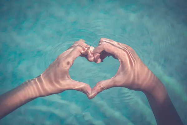 女性は水に手で心の形を作る — ストック写真