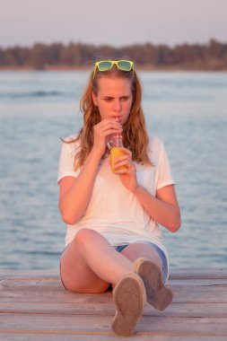 Güzel kadın iskelede oturup ve portakal suyu içme
