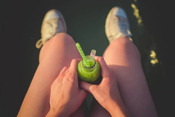 Vrouw met glas groene smoothie op haar knieën — Stockfoto
