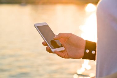 Erkek su yüzey günbatımı arka plan karşı Smartphone kullanarak