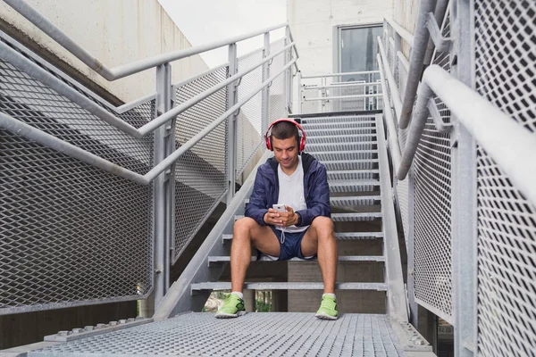 Jogger sentado nas escadas e usando telefone inteligente — Fotografia de Stock