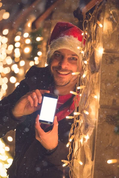 Hombre con pantalla en blanco teléfono inteligente y decoración de luces de Navidad. Concepto de tecnología y vacaciones . — Foto de Stock