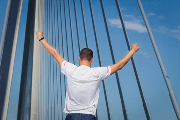 Atlético homem corredor levantou os braços de pé na ponte — Fotografia de Stock