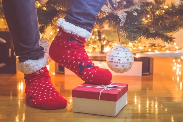Man in reds christmas socks and gift box on floor against decorated Christmas tree background.