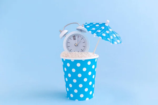 Paper cup full of sand, alarm clock and paper parasol. Sandy beach minimal creative concept. — Stock Photo, Image