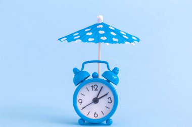 Küçük çalar saat ve kağıt kokteyl polka şemsiye mavi zemin üzerine. Yaz aylarında konsept.