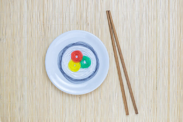 Цветные нити в виде суши на белой тарелке и палочек, изолированных на бежевом бамбуковом соломенном фоне
