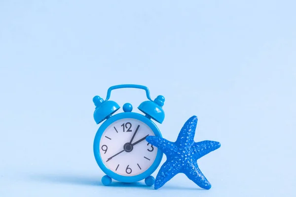 Small alarm clock and sea star isolated on blue. Summer vacation minimal concept. Space for copy. — Stock Photo, Image