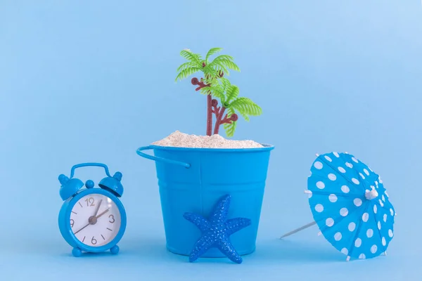 Starfish, paper cocktail parasol, can with sand and plastic palm tree isolated on blue background. Summertime vacation minimalistic still life concept.