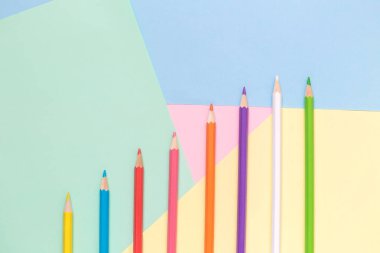 Pastel arka plan minimalist kavramı üzerinde çok renkli kalemler satırda yüksek açılı görünüş.