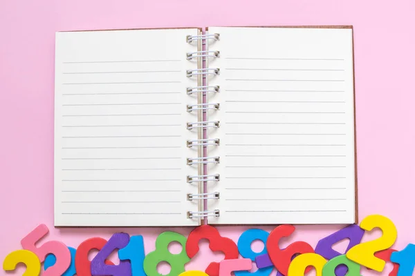 Hochwinkelaufnahme von Notizbuch und bunten Holzzahlen auf rosa Hintergrund minimalistisches Konzept. — Stockfoto