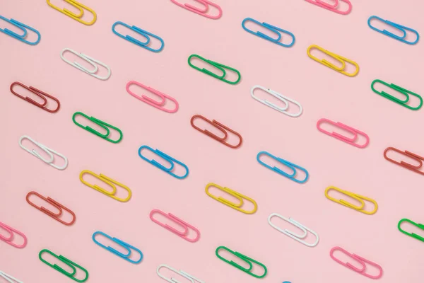 Grampos de papel em cores diferentes contra o conceito de leigos planos minimalistas de fundo rosa . — Fotografia de Stock