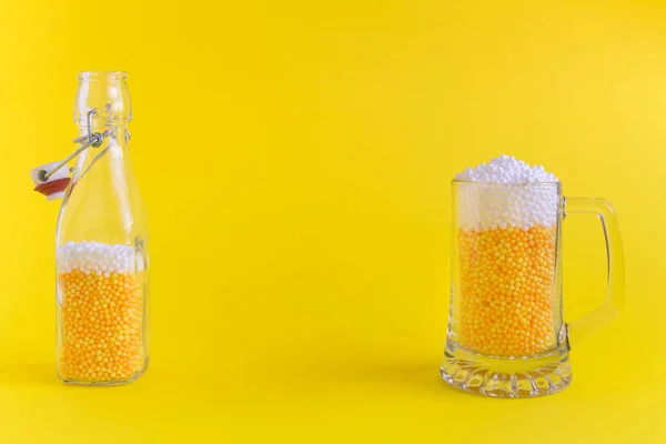 Бутылка и кружка, полные желтых и белых пенных шариков в виде пива минималистская концепция . — стоковое фото