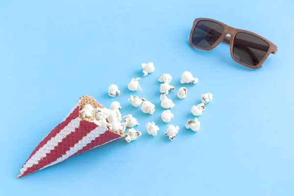 Kegel mit Popcorn und Kinobrille auf blauem Hintergrund minimalistisches Konzept. — Stockfoto