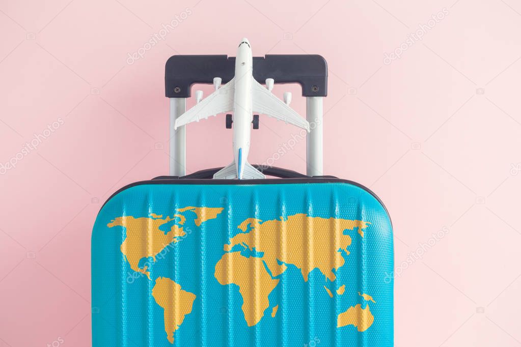 Blue luggage with world continents map and airplane toy on pastel rose background