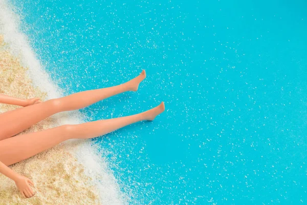 Muñeca piernas tomar el sol en la playa con arena y olas concepto abstracto . — Foto de Stock