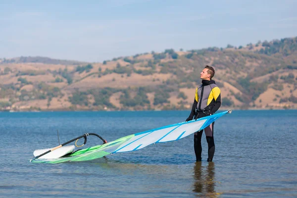 Sportsman en combinaison avec planche de surf et voile attendant le vent . — Photo