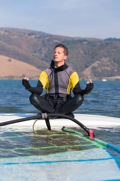 Windsurfer fazendo ioga enquanto sentado na prancha de surf. Esporte e relaxamento conceito . — Fotografia de Stock
