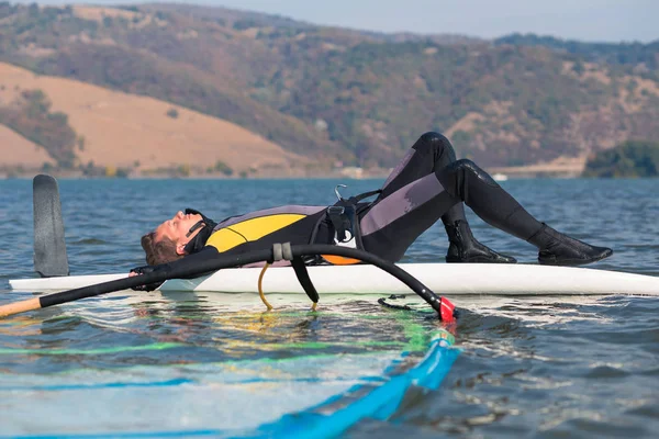 Jovem windsurfista descansando na prancha de surf no oceano. Esporte e conceito de recreação . — Fotografia de Stock