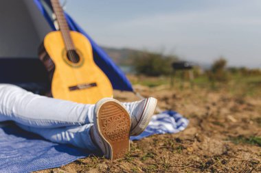 Çadırın önünde akustik gitarın yanına uzanan kadın ayaklarını kapat. Özgürlük ve yaşam tarzı kavramı.
